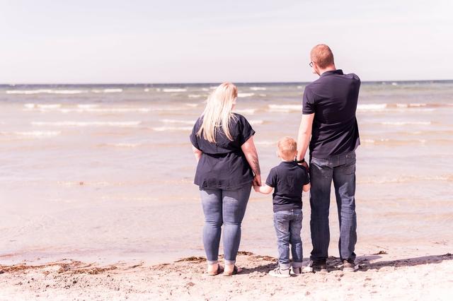 Familie steht Hand in Hand am Strand und blickt auf die Ostsee