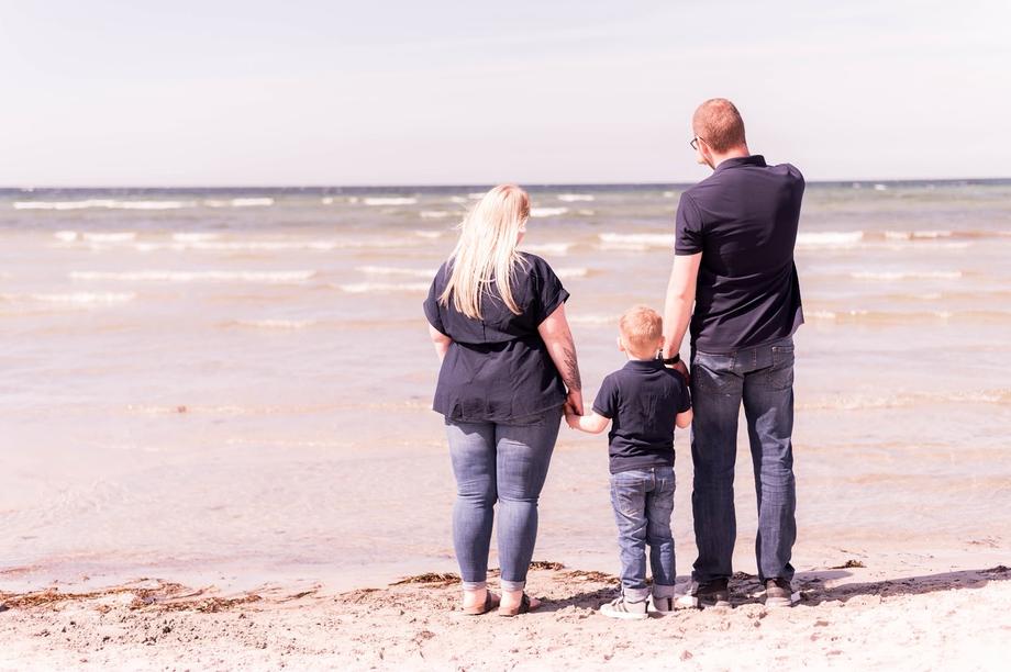 Familie steht Hand in Hand am Strand und blickt auf die Ostsee